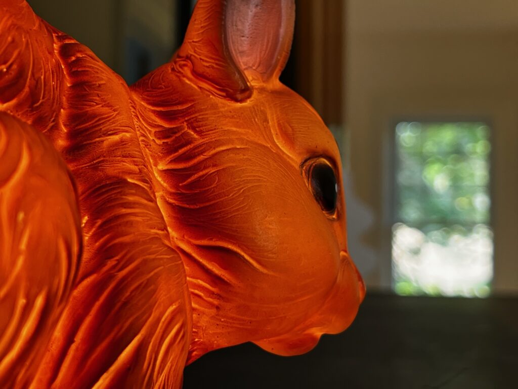 Close up of SquirrelHaus PEC's lighted red squirrel lamp with a window in the background