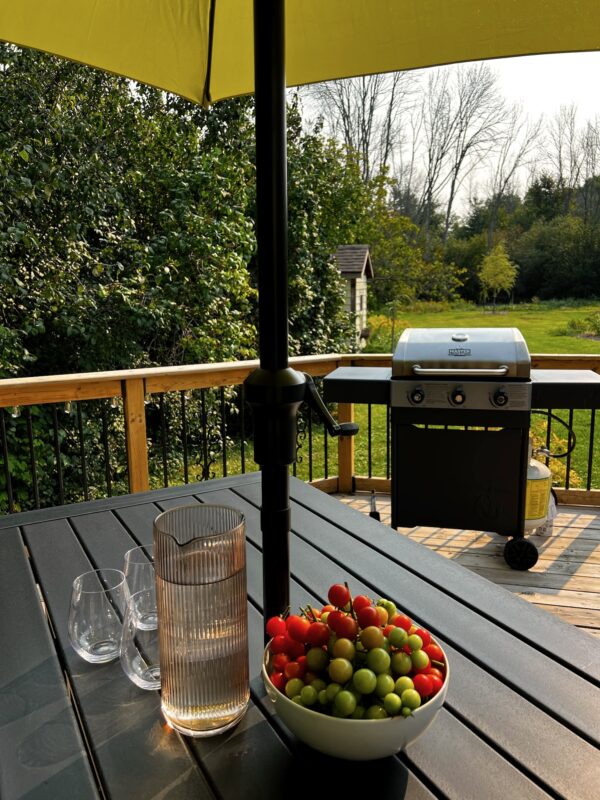 Photo of SquirrelHaus PEC's kitchen deck with a table, grill, a pitcher of water and bowl of cherry tomatoes