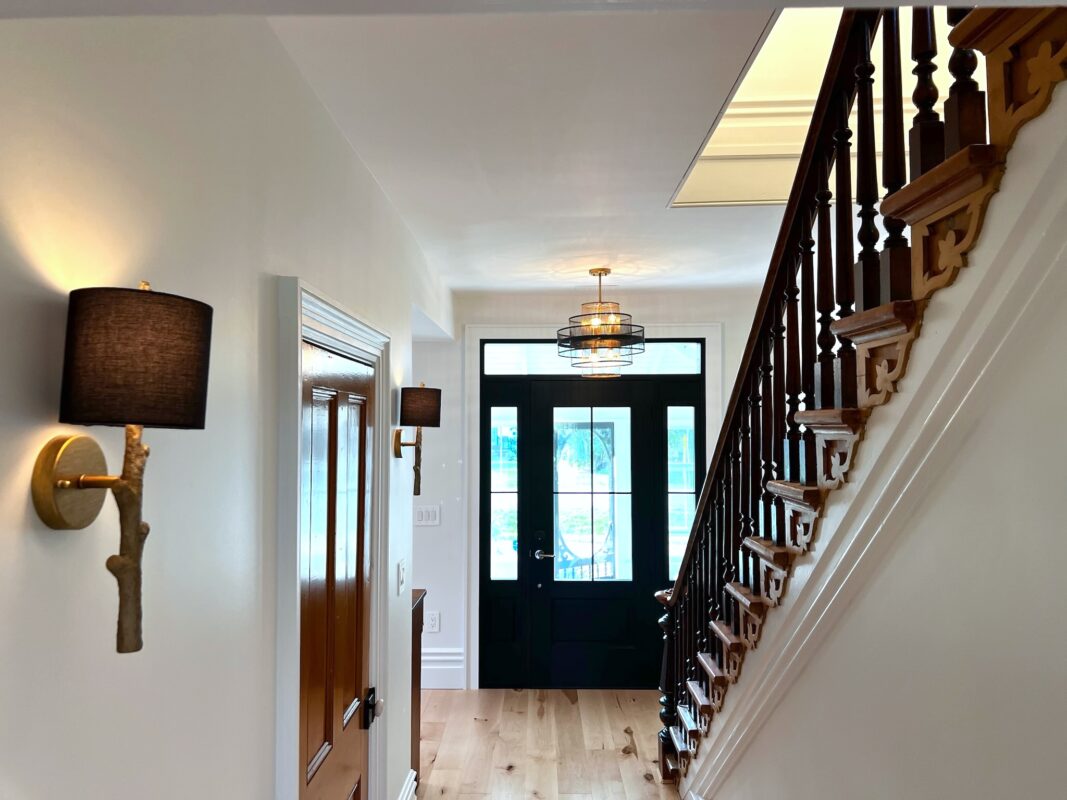 SquirrelHaus PEC's entry hall featuring the original c1900 staircase and pine closet door, wood floors, a large glass door and sconces