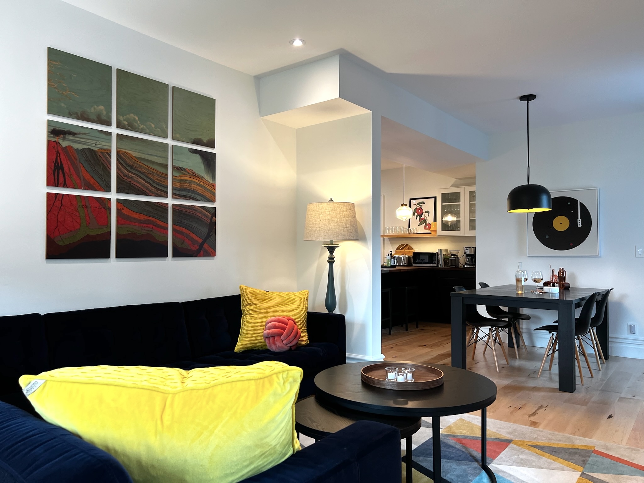 SquirrelHaus' living/dining area. Clean angles. Bright light. Grid wall art. Sofa with colourful pillows.