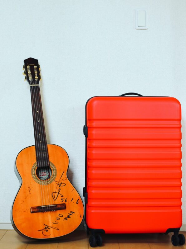 Photo: A signed guitar and clementine roller bag against a blue wall